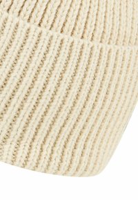 Cream knitted beanie made of soft yarn, featuring a ribbed texture and a slightly slouchy fit. Ideal for casual wear in cooler weather.
