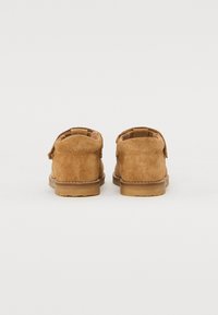 Bruna mockalädersstövlar med rundad tå, låg gummisula och en enkel spänndetalj på sidan. Texturerad yta är synlig.