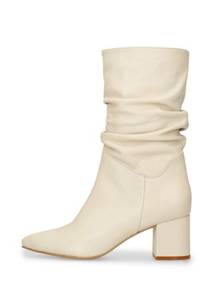 Crèmekleurige leren laars tot halverwege de kuit met een losse schacht, puntige neus en blokhak, zijaanzicht op witte achtergrond.