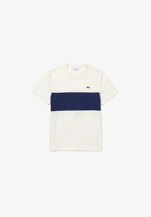 T-shirt blanc à manches courtes avec une large bande horizontale bleu marine sur la poitrine et un petit logo crocodile vert sur le côté gauche.