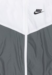 White and gray Nike jacket with central white zipper and black Nike logo on the upper right chest area.