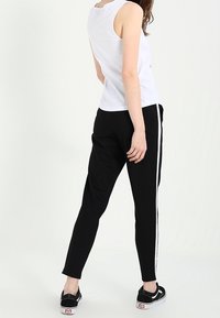 Vit ärmlös linne topp kombinerad med svarta avsmalnande byxor med vita sidostreck. Modellen bär svarta sneakers.