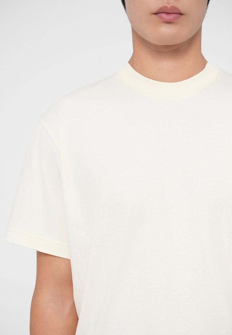 Camiseta de manga corta de color amarillo claro, hecha de algodón suave. Presenta un escote redondo con un sutil detalle acanalado. Textura suave en general.