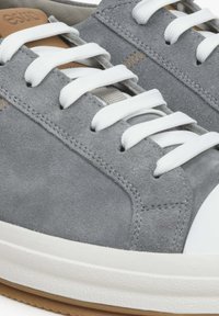 Szare zamszowe sneakersy z białymi sznurowadłami, gładką osłoną noska i teksturowaną gumową podeszwą. Projekt zawiera subtelne przeszycia oraz brązowy akcent.