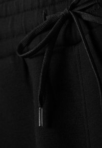 Μαύρο φούτερ παντελόνι με λεία υφή, που διαθέτει ρυθμιζόμενο κορδόνι και ασημένιο μεταλλικό διακοσμητικό στο τέλος του κορδονιού.