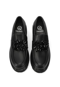 Mocassini in pelle nera con una finitura lucida, caratterizzati da una larga fascetta decorata con dettagli simili a cristalli neri. Punta arrotondata e suola spessa.
