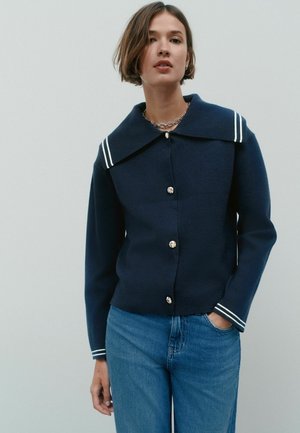 Marineblauer Jacke aus Wollmischung mit großem Kragen, der weiße Streifen am Kragen und an den Manschetten sowie silberfarbene Knopfverschlüsse aufweist.