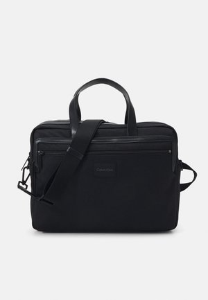 Borsa in tessuto nera con due manici superiori e una tracolla regolabile. Presenta scomparti con zip e un'etichetta con logo sul davanti.