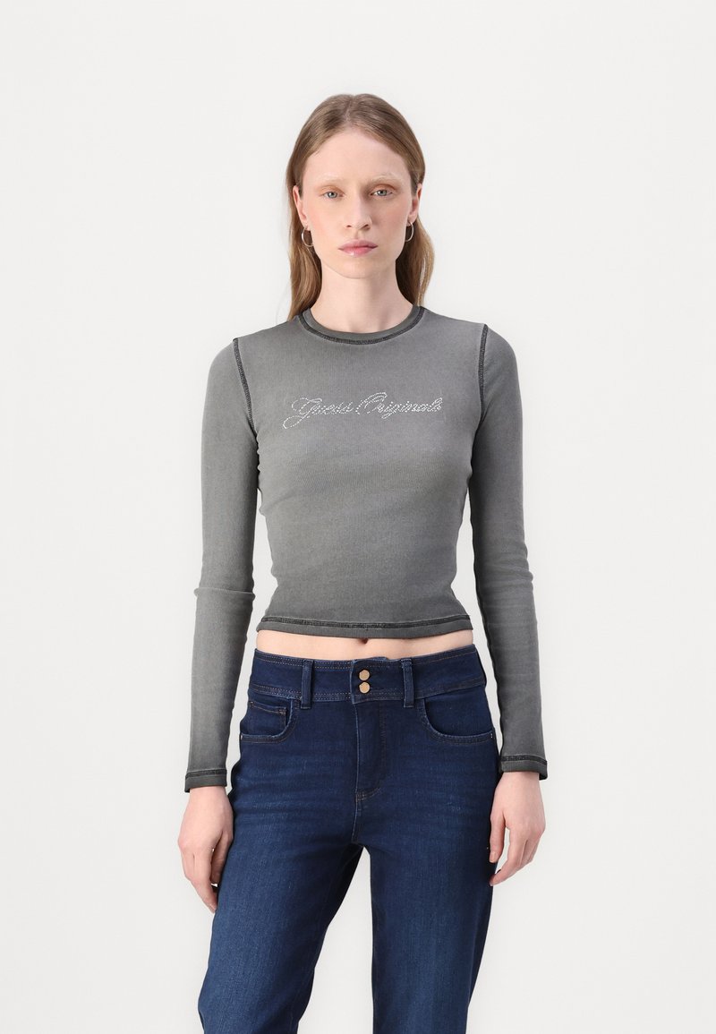 Grå, langermet cropped skjorte med kontrastsøm og tekstdekorasjon foran; parret med mørkeblå denimjeans med knappelukking.