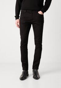 Pantalon slim noir en denim, doté d'une poche avant, de couture contrastante, associé à des bottines noires.