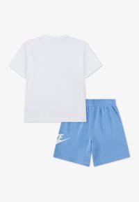 Λευκό βαμβακερό μπλουζάκι με κοντά μανίκια σε συνδυασμό με μπλε βαμβακερό σορτς που διαθέτει μεγάλο λευκό λογότυπο Nike στην αριστερή πλευρά.