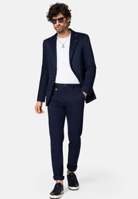 Granatowa marynarka na białej koszulce, zestawiona z granatowymi spodniami. Dodatki to okulary przeciwsłoneczne i naszyjnik, a do całości pasują ciemne sneakersy.
