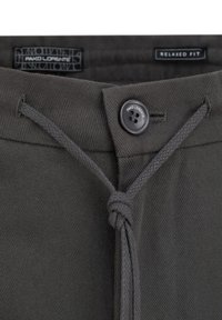 Ciemnozielone, luźne spodnie z zapięciem na guziki, detalem w postaci sznurka i teksturowanym materiałem. Metki widoczne blisko pasa.