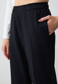 Schwarze Jogginghose mit elastischem Bund und Seitentaschen. Glatte Textur mit subtilen Stickdetails. Ideal für angenehmen Tragekomfort.