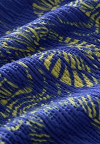 Tissu texturé avec une base bleue et un motif jaune ondulé, présentant une surface froissée et des couleurs vives.