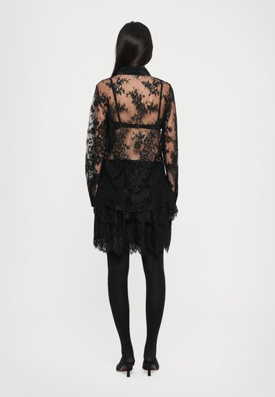 Svart blondekjole med gjennomsiktig bodice, lange ermer og tiered volanger i kanten. Har delikate blomster mønstre og en tettsittende silhuett.