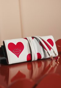 Portefeuille en cuir blanc avec de grands cœurs rouges et un graphic de lèvres. Il possède deux zips avec des charms en forme de cœur, affichant une surface texturée.