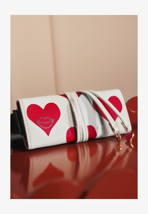 Portefeuille en cuir blanc avec de grands cœurs rouges et un graphic de lèvres. Il possède deux zips avec des charms en forme de cœur, affichant une surface texturée.