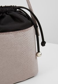 Torba typu bucket z teksturowaną, jasnoróżową bazą, czarnym ściągaczem oraz srebrną kulką ozdobną na końcu paska.