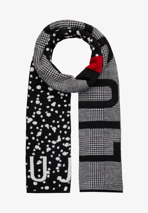 Écharpe à motifs noir et blanc avec des blocs et des motifs pied-de-poule, des taches blanches éparpillées, et un petit patch rouge près du sommet.