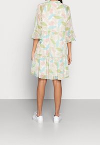 Kukalliskuvioinen mekko, jossa on kerroksittainen malli, pastellivärit (vaaleanpunainen, vihreä, sininen) ja röyhelöhihat, yhdistettynä valkoisiin tennareihin.