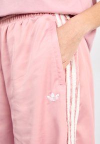 Rosa satinidrottshorts med elastiskt midjeband, sidoficka och vita randiga detaljer. Har broderad logotyp på benet.