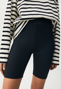 Gros plan sur une personne portant un short de cyclisme ajusté noir et un haut à manches longues ample beige rayé de noir.