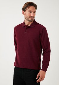 Bordeaux-langarm-Polohemd mit weicher Textur, klassischem Kragen und doppelter Knopfleiste, kombiniert mit schwarzen Hosen.