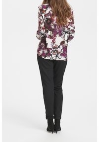 Blusa de manga larga en tejido crema con un diseño floral en púrpura y negro, combinada con pantalones negros y botas till ankle.