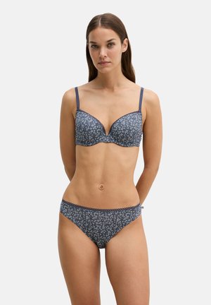 Woman facing forward wearing matching navy blue floral print bra and briefs on plain light background.