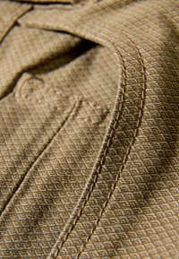 Tessuto beige con trama a quadretti. L'immagine mostra cuciture dettagliate lungo le cuciture e una tasca visibile.