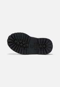 Semelle en caoutchouc noir avec des rainures profondes et un motif étoilé pour une meilleure adhérence. Présente le logo Timberland embossé sur le côté pour une touche de détail supplémentaire.