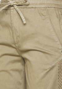 Bermudas de tom bege claro com cintura elástica, cordão ajustável e detalhe em painel lateral texturizado. Feitas de um tecido suave e liso.
