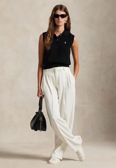 Melna bezroku polo krekls ar mazu logotipu, kopā ar augsta vidukļa baltām biksēm. Aksesuāri: melna soma un balti sporta apavi.