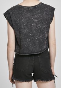 Camiseta corta de acid wash negra con mangas cortas, combinada con pantalones cortos de mezclilla negros con dobladillos deshilachados y detalles de cordones en los lados.