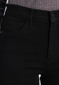 Black denim jeans with a fitted design, featuring five-pocket style, belt loops, and a smooth texture. The button closure is visible.