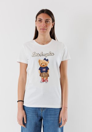 T-shirt in cotone bianco con una grafica di un orso in camicia blu con una bandiera americana, che indossa una gonna e sneaker rosse, con la scritta "Los Angeles".