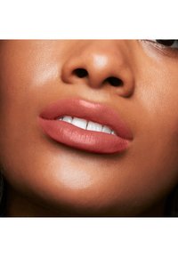 Couleur de rouge à lèvres matte dans une teinte rose nude, mettant en valeur une texture lisse et des lèvres bien définies. La peau présente une lueur chaude et radieuse.