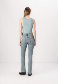 Top de bumbac ușor, de culoare albastru deschis, cu dungi, purtat cu blugi din denim deschis, ajustați. Blugii au talie înaltă, buzunare la spate și detalii cu margini desfăcute.