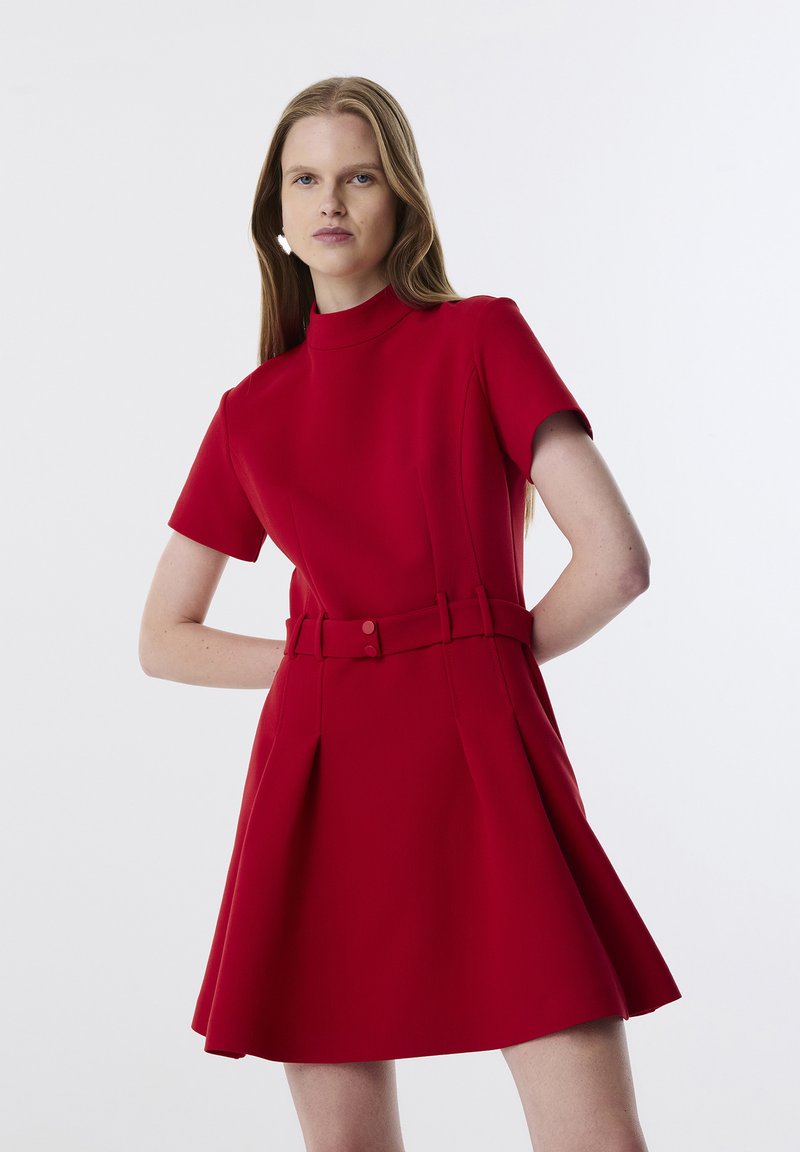 Abito rosso a maniche corte con scollo alto, corpino aderente e gonna svasata. Presenta una cintura in vita con bottoni decorativi. Tessuto dalla superficie liscia.