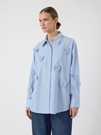 Striped blue button-up shirt with floral appliqué accents, long sleeves, and a collar. Made from lightweight fabric, has a relaxed fit.