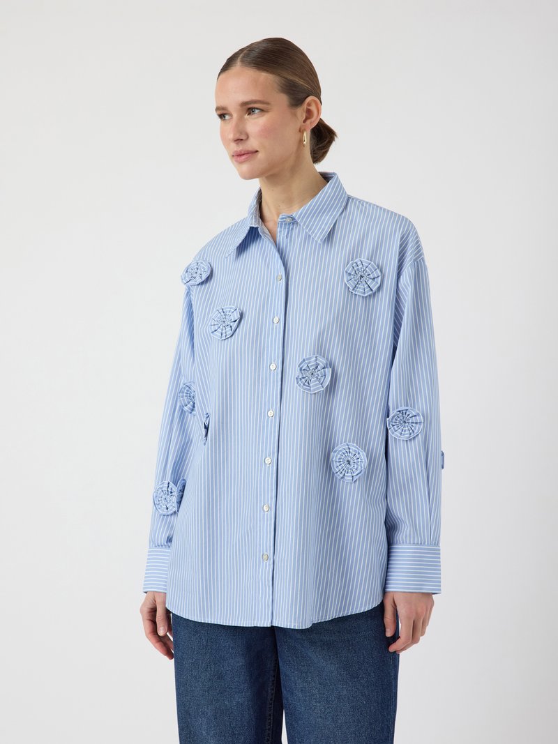 Striped blue button-up shirt with floral appliqué accents, long sleeves, and a collar. Made from lightweight fabric, has a relaxed fit.