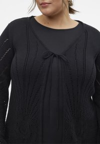 Mustat neulotut neuletakit, joissa on V-muotoinen kaula-aukko, solmimisvyö etuosassa ja avonaisia kuvioita hihansuissa ja vartalossa.