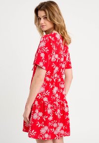 Robe rouge à manches courtes, avec des motifs floraux blancs, taille cintrée et jupe à volants. Fabriquée en tissu léger, texture douce.