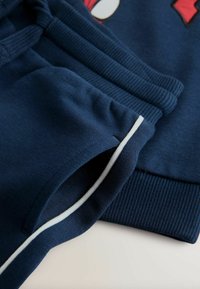 Ensemble de sweat à capuche et de pantalons de jogging bleu marine avec des poignets côtelés, des poches latérales et des bandes blanches le long des bords du pantalon.