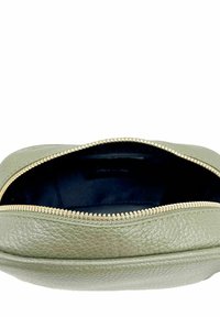 Bolso de cuero verde claro con un acabado texturizado, que presenta una cremallera dorada y un interior azul marino. La parte superior abierta muestra el compartimento interior.