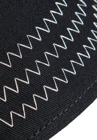 Tissu noir avec des coutures en zigzag blanches. La vue rapprochée met en évidence la texture et le détail du motif de couture.