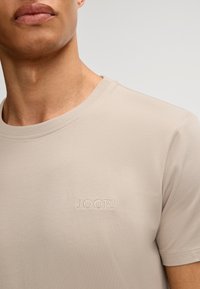 Beige crewneck t-shirt lavet af blødt bomuldsstof. Har et broderet "JOOP!" logo på venstre side af brystet. Glat tekstur og tætsiddende design.