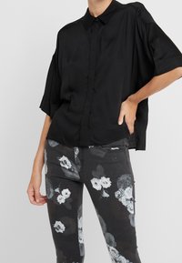 Zwarte kortekorte mouwen overhemd met knopen, gemaakt van gladde stof. Gepaard met donkere skinny jeans met een bloemenpatroon, met witte en grijze rozenontwerpen.