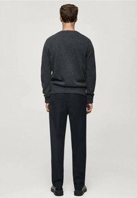 Dunkelgrauer, gestrickter Pullover mit rundem Ausschnitt, kombiniert mit schwarzen, maßgeschneiderten Hosen und schwarzen Schuhen, von hinten betrachtet.